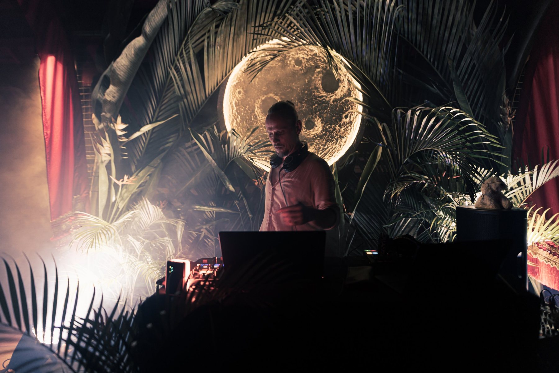 Acharya DJing in front of a moon and palm-leaf stage design