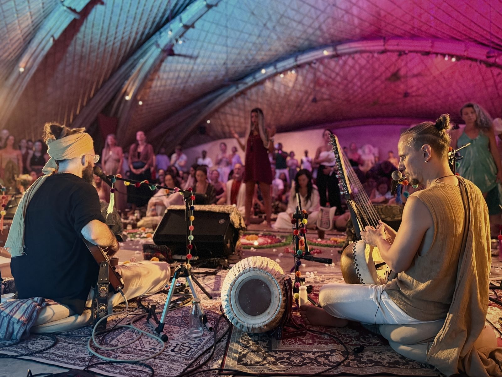 Acharya playing a string instrument on stage with Hanuman Project, a crowd gathered under a lit dome